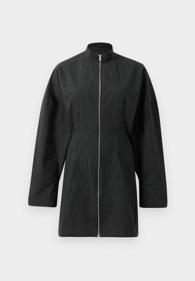 Svart jacka med hög krage, frontdragkedja och lös passform. Har ett texturerat mönster med rutdesign och något överdimensionerade ärmar.