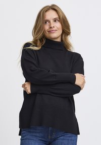 Fekete garbó pulóver bordázott mandzsettákkal �és aljjal, laza fazonnal és oldalsó hasítékokkal. Farmernadrágra van húzva.