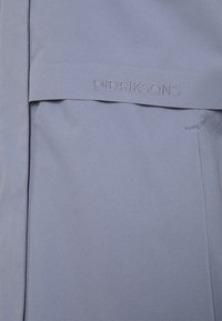 Tissu Didriksons bleu clair avec une texture lisse, présentant le nom de la marque brodé sur un rabat, design minimaliste aux lignes épurées.