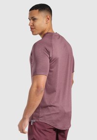 Sportovní tričko s krátkým rukávem v burgundské barvě, vyrobené z texturované tkaniny a s kulatým spodním lemem, oblečené s vínovými šortkami, s bočním profilem.