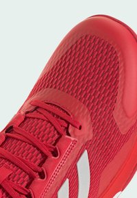 Baskets de sport rouges avec un dessus en tissu texturé, accents en caoutchouc lisse, lacets plats et un détail de logo réfléchissant.