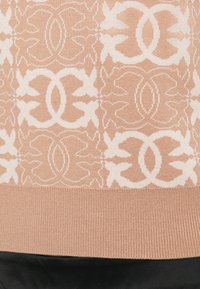 Pull de malha com uma base de pêssego claro e padrões geométricos florais brancos. Barra canelada e tecido preto contrastante na parte inferior.