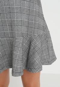 Jupe à carreaux noir et blanc avec un ourlet évasé, présentant un tissu texturé et des motifs de carreaux variés, y compris des accents de pied-de-poule.