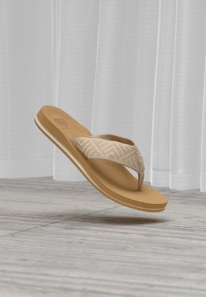 Καφέ σαγιονάρα με λουράκι από υφασμάτινο σχέδιο που αιωρείται πάνω από πάτωμα από ανοιχτό ξύλο και λευκές διαφανείς κουρτίνες στο φόντο.