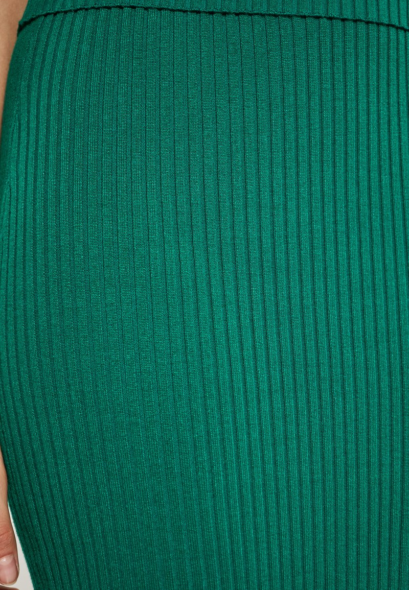 Groene ribstof met verticale lijnen, voorzien van een zachte textuur en een aansluitend ontwerp. Close-upzicht benadrukt textuur en kleur.