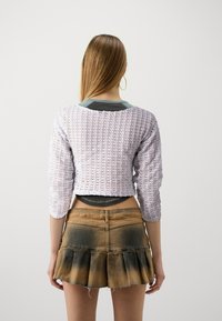 Top scurt de culoare lavandă, croșetat, cu mâneci trei sferturi, asortat cu o fustă mini din denim, cu un tiv volanat în straturi și culori gradient.