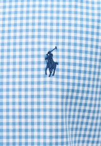 Sinine ja valge ruuduline kangas tumeda sinise tikandiga, mis kujutab ratsutavat polo mängijat, kes hoiab malletti.