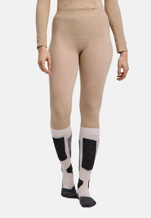 Persoon draagt beige naadloze legging en witte kniehoge sokken met zwarte geometrische patronen, loopt vooruit tegen een effen achtergrond.