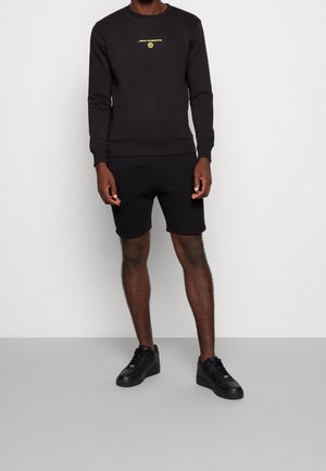 Svart sweatshirt med rund hals och långa ärmar, prydd med en gul "New Horizon"-logotyp. Matchas med svarta shorts och svarta sneakers.