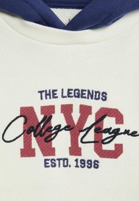 Un hoodie blanc avec des accents bleu marine et un texte brodé. Il présente "NYC" en gras maron, "College League" en cursive et l'année d'établissement 1996.
