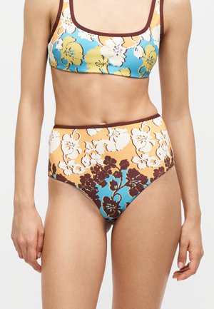 Femme portant un bas de bikini taille haute et un haut assorti avec un imprimé floral multicolore et une bordure marron.