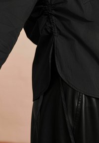 Bluză neagră cu cusături laterale pliate, tiv curbat și un material neted, texturat. Asortată cu o fustă elegantă din piele neagră.