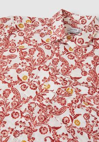 Camicia bianca con un motivo floreale rosso e giallo, dotata di colletto, chiusura con bottoni e tessuto testurizzato. Dettagli floreali presenti in tutto il capo.