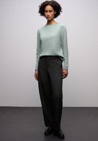 Jasnozielony, długi sweter z dekoltem typu łódka; zestawiony z ciemnymi, szerokimi spodniami i czarnymi botkami, tworzącymi swobodną sylwetkę.