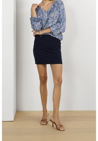Dlouhá modrá květinová blůza s výstřihem do V, doplněná černou obepínající minisukní a hnědými sandály na podpatku.