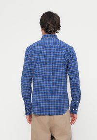 Blue plaid button-up shirt with long sleeves, featuring white grid lines and a standard collar. Fabric appears smooth; back includes a yoke seam.