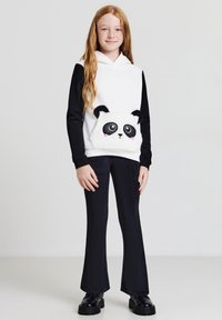 Felpa con cappuccio dalle maniche nere e corpo bianco, caratterizzata da un dettaglio di un viso di panda soffice. Abbinata a pantaloni neri a campana e scarpe nere.