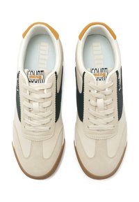 Zapatillas beige de cuero suave con paneles laterales verdes, punta redonda y detalles en marrón claro en el talón. Incluyen cordones y suela texturizada.