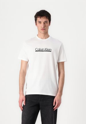 Tricou alb din bumbac, cu guler rotund, având un logo negru "Calvin Klein" centrat pe piept. Mâneci scurte și croială lejeră.