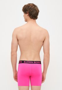 Roosa bokserite aluspesu musta elastse vööga, millel on paksude tähtedega brändinimi "BJÖRN BORG". Sile tekstuur ja kitsas disain.