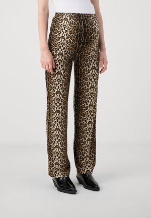Pantalon droit imprimé léopard porté avec des bottines noires à bout pointu et un haut blanc sur un fond uni.