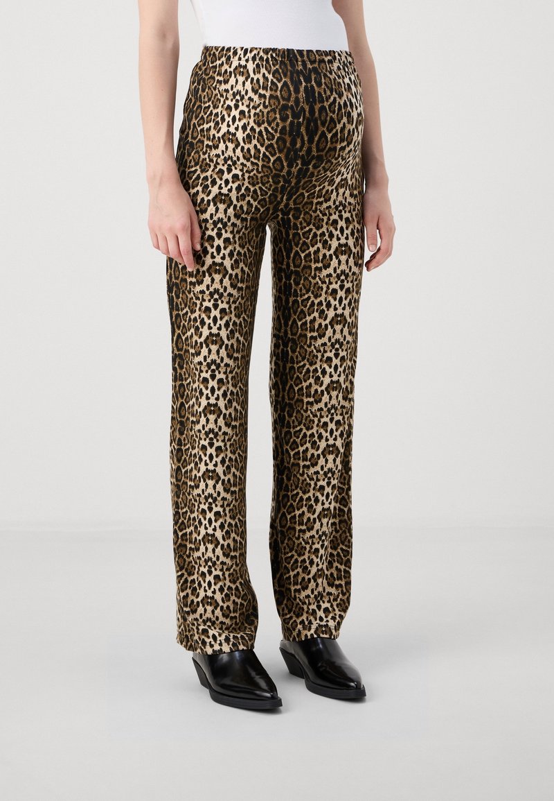 Pantalon droit imprimé léopard porté avec des bottines noires à bout pointu et un haut blanc sur un fond uni.