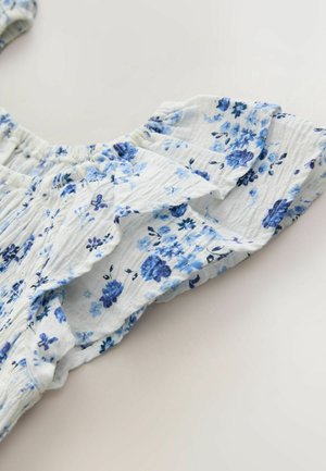 Vaaleansinisestä ja valkoisesta kankaasta valmistettu kukallinen pusero. Siinä on kerätyt röyhelöhihat, joissa on pieniä sinisiä kukkakuvioita, kevyt rakenne.