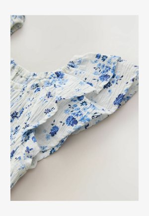 Kvetinová blúzka z ľahkej modro-bielej tkaniny. Má nariasené volánové rukávy s malými modrými kvetinovými vzormi, ľahkú textúru.