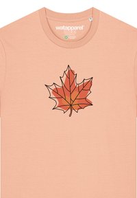 Lichtroze t-shirt met een grafische afbeelding van een esdoornblad in oranje en rode tinten met een zwarte omtrek, gemaakt van zachte stof.