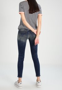 Úzké džíny v tmavě modrém denimu s efektem vyblednutí, spárované s tričkem s černobílými pruhy a bílými teniskami.