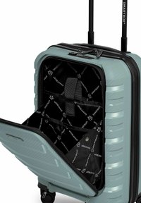 Valise rigide avec compartiment avant zippé ouvert, révélant un intérieur noir avec logos de la marque et poignée réglable étendue.