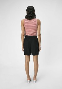 Rød og hvid stribet ærmeløs top, sorte shorts med elastisk talje, let stof og hvide hælede sandaler. Set fra ryggen.