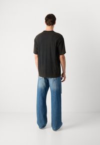 Juodas medvilnės T shirt su trumpomis rankovėmis ir apvaliu kaklu, derinamas su šviesiai mėlynomis plačiomis kelnėmis, pasižyminčiomis gradientiniu plovimu ir užpakalinėmis kišenėmis.