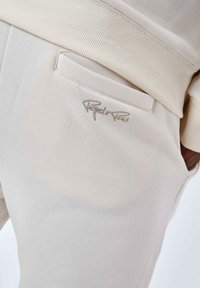 Pantaloni sportivi beige chiaro con coulisse a costine, dotati di una tasca cucita e dettaglio del logo ricamato nello stesso tono sul lato.