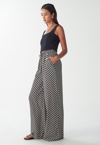 Black ribbed tank top paired with patterned wide-leg trousers in cream and black, featuring pockets and a tied waist. Smooth fabric finish.