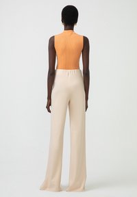 Body ribbed portocalie fără mâneci, asortat cu pantaloni largi bej, cu talie înaltă; textură netedă și croi adaptat pentru un look modern.