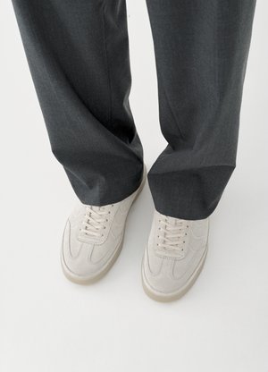 Béžové semišové tenisky s okrúhlou špičkou, šnurovacím systémom a textúrovanými panelmi, skombinované s tmavosivými nohavicami vo voľnom strihu.