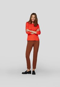 Red button-up shirt with long sleeves and brown slim-fit pants, complemented by black loafers, against a neutral background.