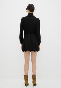 Pull à col roulé noir à manches longues associé à une jupe plissée noire avec une fermeture éclair dorée au dos. Bottines en daim.