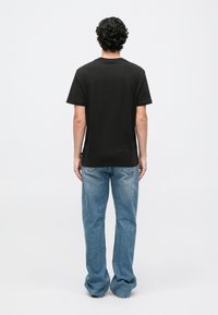 T-shirt de algodão preto com mangas curtas, apresentando um decote redondo. Usado com jeans de ganga azul claro. Design simples, sem adornos.