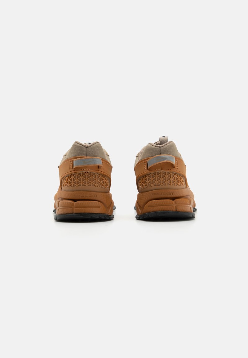 Bruine en beige sportschoenen met een gestructureerde bovenkant, mesh-details en een patroon aan de zijkant. Rubberen zool met zwarte loopvlak.