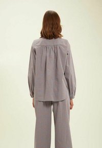 Chemise à carreaux en tissu léger, dotée d'un dos plissé, de manches longues et d'un ourlet arrondi. Les couleurs incluent rouge, bleu et blanc.