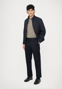 Granatowa pikowana kurtka na teksturowanym, jasnoszarym swetrze, zestawiona z ciemnymi spodniami i czarnymi butami, tworząca uporządkowany, monochromatyczny wygląd.