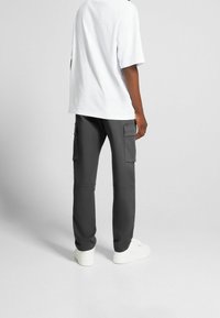 Grå cargobyxor med sidofickor, rak skärning, tillverkade av lättviktsmaterial, i kombination med en löst passande vit t-shirt.