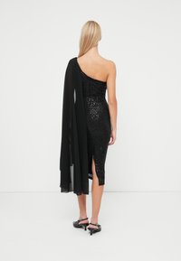 Čierne šaty na jedno rameno so sequins, s voľným plášťom na jednej strane, po kolená a so štrbinou na pravej strane.