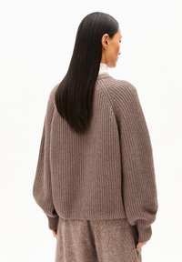 Gebreide trui in zacht bruin met ribbelstructuur en oversized pasvorm. Heeft wijde mouwen en een hoge kraag. Geschikt voor layering.