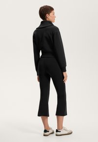 Sweat-shirt noir court avec un col et des poignets ajustés, associé à un pantalon noir court. Complété par des baskets blanches et vertes.