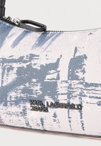 Τσάντα από faux δέρμα με υφή σε λευκό χρώμα με μπλε αφηρημένα σχέδια. Διαθέτει μαύρο φερμουάρ και μεταλλική πλακέτα με το λογότυπο "KARL LAGERFELD JEANS".