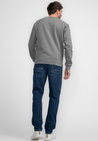 La felpa grigia presenta polsini e orlo a coste, abbinata a jeans blu scuro e sneakers bianche, che mostrano una vista laterale casual.