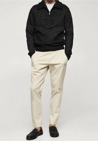 Schwarzer Strickpullover mit Reißkragen, cremefarbene Hose und schwarze Slipper, mit strukturiertem Muster und lockerer Passform.